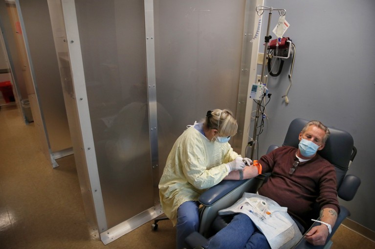 A nurse prepares to treat a man sitting in a clinical chair.