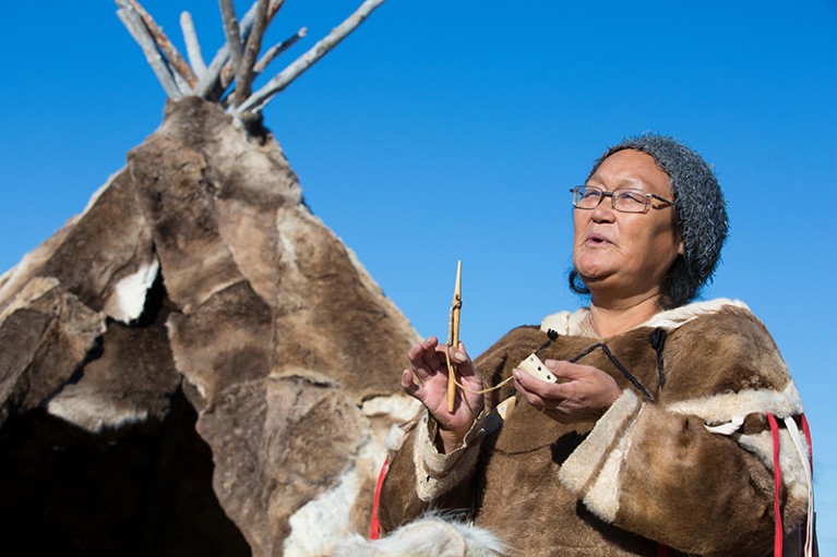 In Arviat, Nunavut, Canada, a local woman demonstrates historic tools used by Inuit, with a polar tent in background.