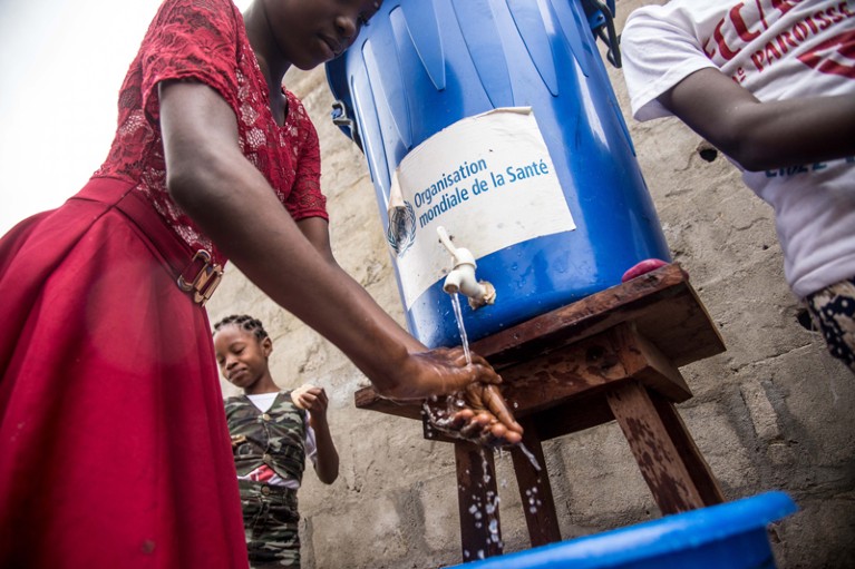 A woman washes her hands from a tank of water bearing a World Health Organization sticker, as a prevention against Ebola