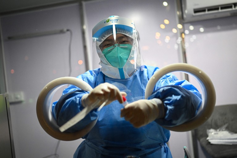 An employee wearing a hazmat suit holds a swab sample through holes in a perspex screen in Beijing