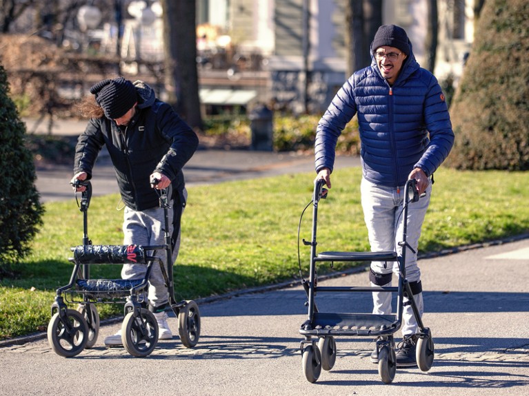 People with spinal-cord injuries walking outside while supported on walking frames..