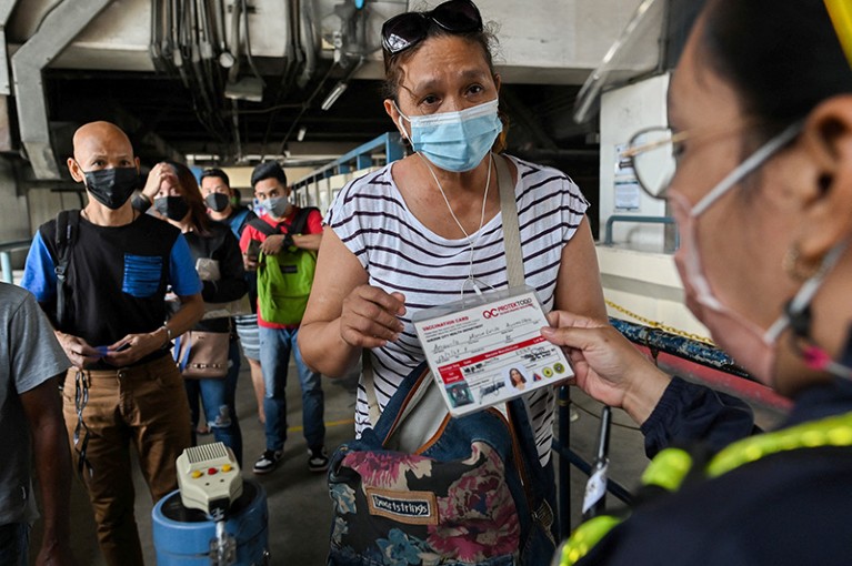 A woman in a face mask presents her vaccination card as the Philippine capital limits public transportation to the vaccinated.