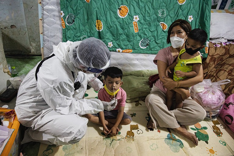 在泰国曼谷，一名穿着个人防护装备的志愿者正在从一名儿童身上提取鼻拭子样本，以检测Covid-19。