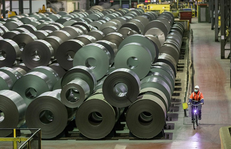 A worker rides a bike by steel coils in storage at the steel factory of German corporation ThyssenKrupp in Duisburg, Germany.