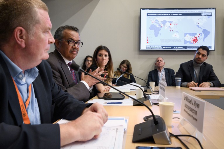World Health Organization officials lead a press conference on the COVID-19 pandemic showing case numbers on a map on a monitor