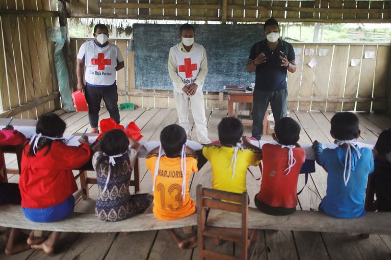 Personnel from the Peruvian Red Cross speak to a line of schoolchildren sitting at a table