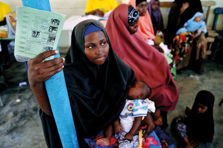 A young mother clutches her baby while standing in a queue