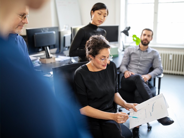 Businesswoman pointing at a statistical report and discussing with colleagues in office.