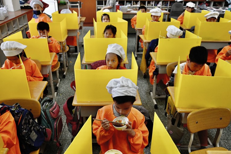 Children in Taiwan eat lunch at classroom desks fitted with yellow plastic partitions to prevent the spread of COVID-19