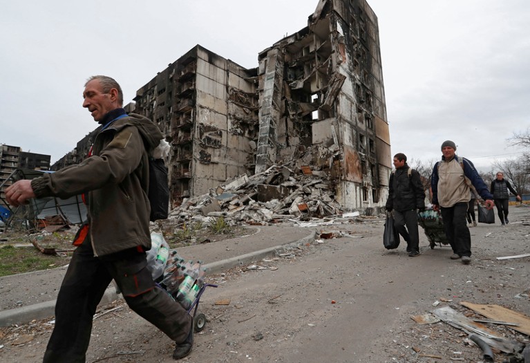 Local residents or Mariupol carry luggage as they walk past a high-rise building destroyed during Ukraine-Russia conflict