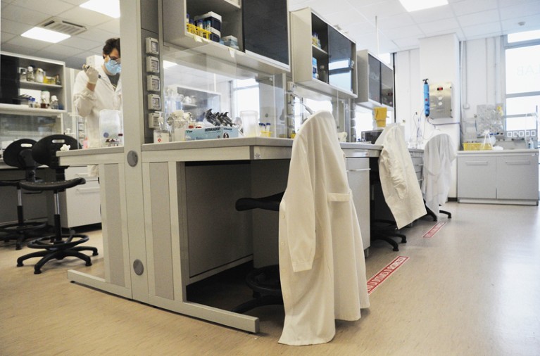 Lab coats of scientists are left on empty chairs in a lab