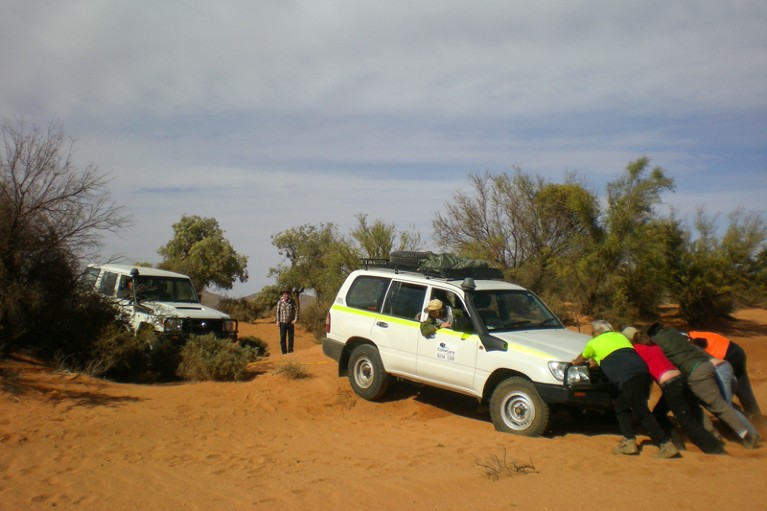 People pushing a 4x4 truck in a sandy area