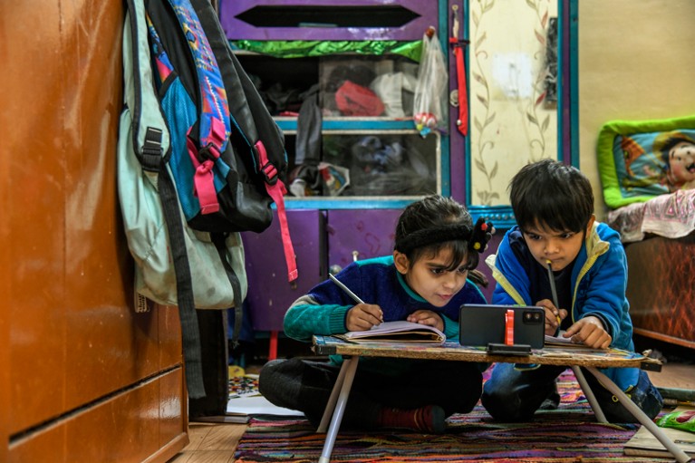 在印度的一节在线课上，两个孩子一边在笔记本上写字，一边盯着手机