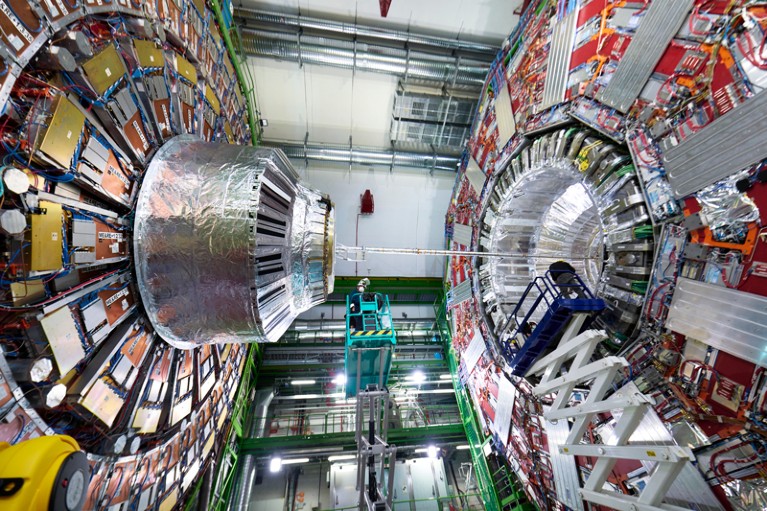 An engineer stands high on a cherry picker between two parts of the CMS detector during the Long Shutdown 2 at CERN