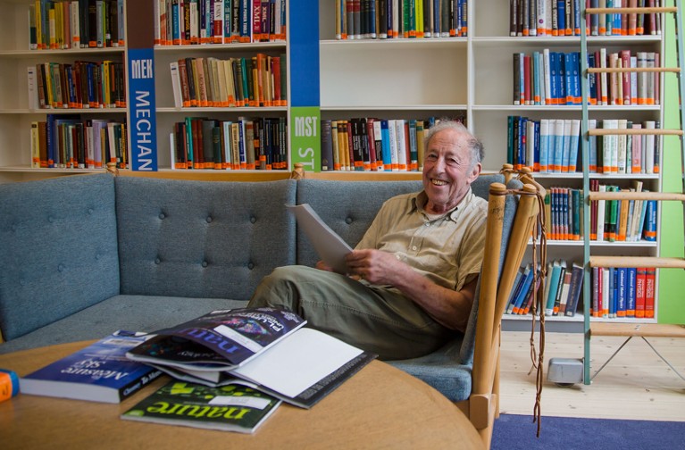 Portrait of Ben Mottelson sitting on a sofa with bookshelves behind him