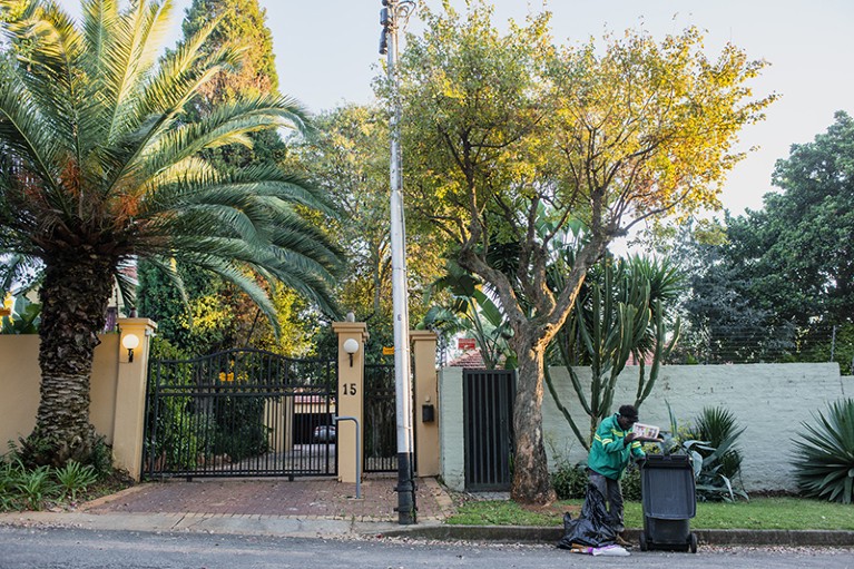 在南非约翰内斯堡一个富裕的郊区，一个捡垃圾的人在一所有大门的住宅外整理一袋垃圾。