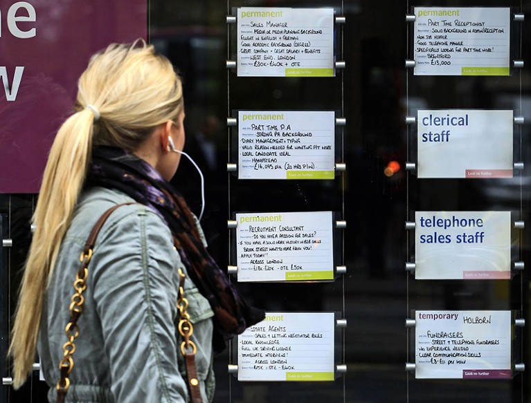 在英国伦敦，一名女子正在一家招聘机构的橱窗里查看招聘启事