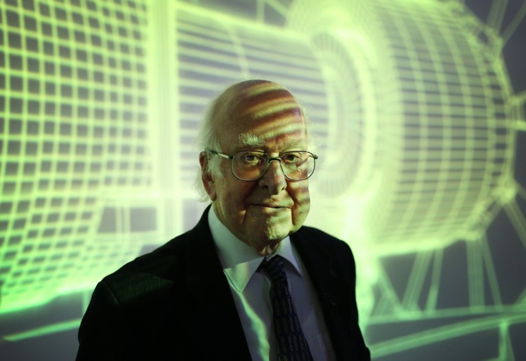 Peter Higgs stands in front of a Large Hadron Collider art projection
