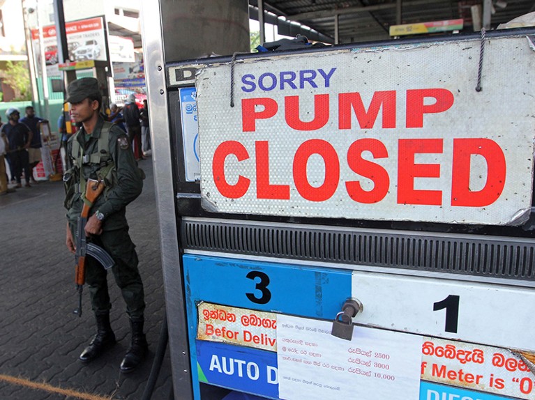 Sri Lankan security personnel stands guard outside a fuel station with a sign reading 'Sorry, pump closed'.