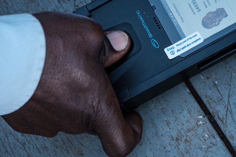 在坎帕拉的一个投票站，一名男子将拇指放在生物识别机器上，检查他的身份证，以便投票
