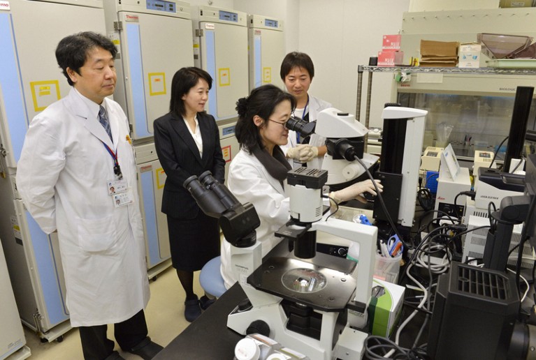 Researchers watch another researcher carrying out an experiment under a microscope in the lab