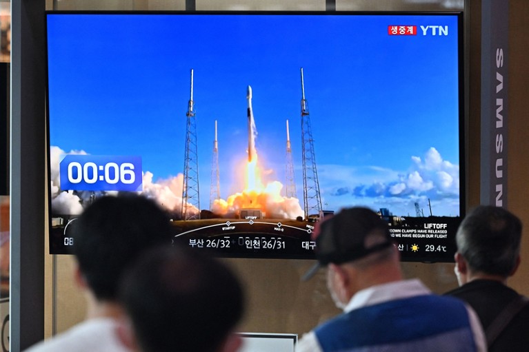 People watch a television screen showing live footage of the launch