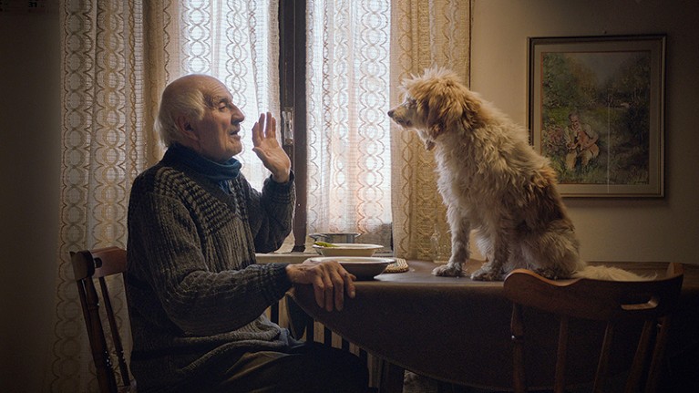 Man with dog indoors in a scene from the 2020 documentary, The Truffle Hunters.