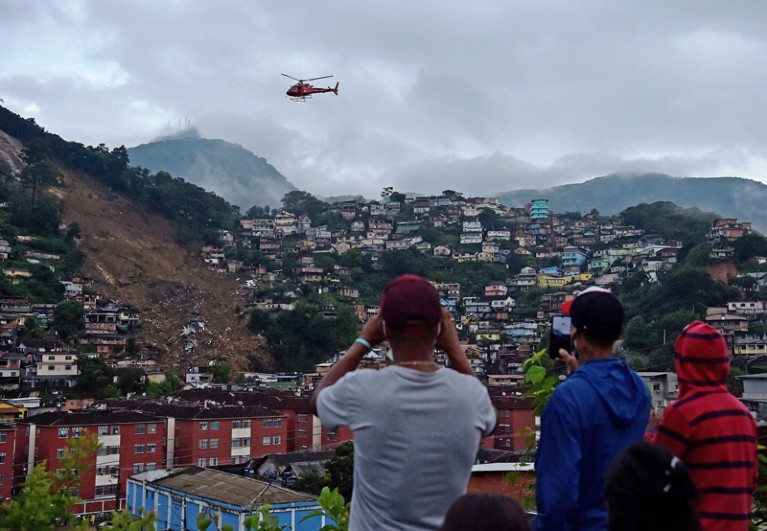 在巴西的彼得罗波利斯，人们看着一架紧急服务直升机飞过一个巨大的滑坡