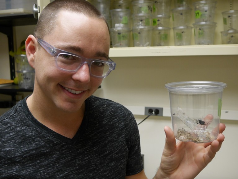 Jonathan Pruitt holding a clear plastic pot containing a spider
