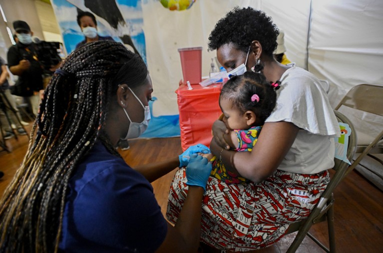 A mother holds her one-year-old daughter as she receives a Pfizer COVID-19 vaccination from a health are worker