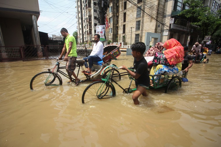 Rickshaw pullers transport customers along a knee-high flooded street