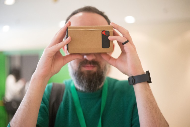 A man holds up a cardboard virtual reality head set containing a phone to his eyes