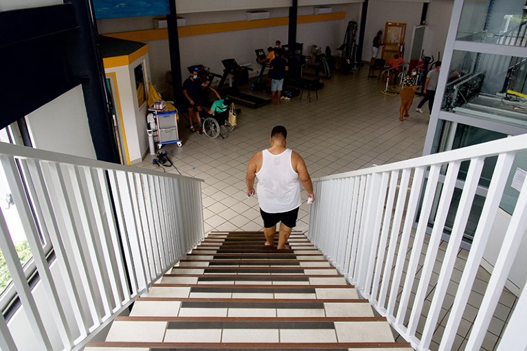 A man in a tank top and shorts walks down a flight of stairs towards a waiting room