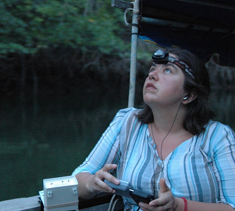 Kate Jones looks up while using equipment to record bat acoustics on a river in Thailand
