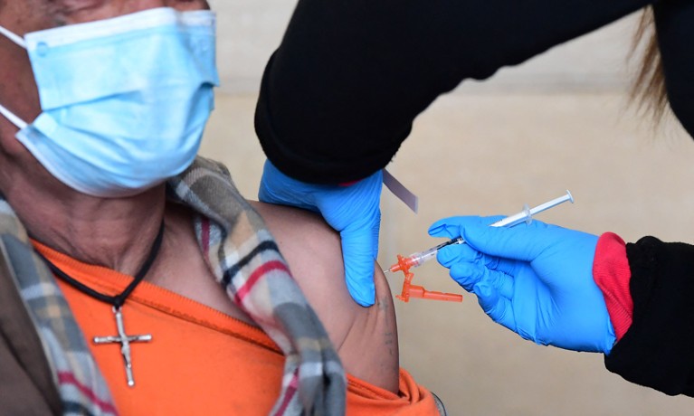 Close-up of a man in a surgical mask receiving a vaccine against COVID-19.