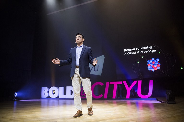 Xun-Li Wang stands on stage, delivering a talk at CityU’s BOLD Forum