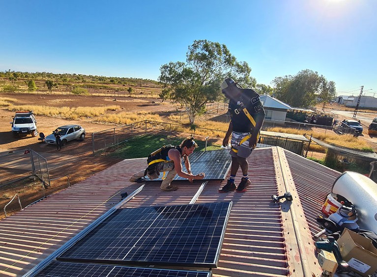 Two people installing solar panels on the roof of a house in Tennant Creek