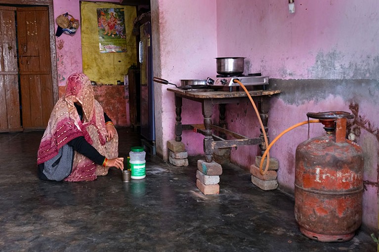 A woman sits on the floor near a stove connected to a liquefied petroleum gas (LPG) cylinder at a home in Greater Noida, India