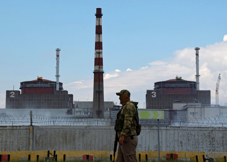 A serviceman with a Russian flag on his uniform stands guard in front of the Zaporizhzhia Nuclear Power pPant