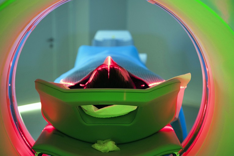 A patient lies on a bed inside a scanning machine lit with colourful lights