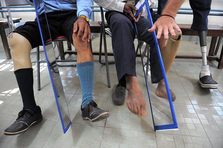 View of two seated amputees holding a mirror up to their biological leg during a therapy session