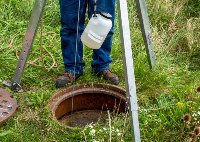 Close up photo of a wastewater engineer retrieving a sampling container from a manhole