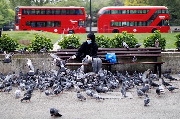 A woman wearing a face mask feeds pigeons in an almost deserted Marble Arch in London on April 27, 2020.