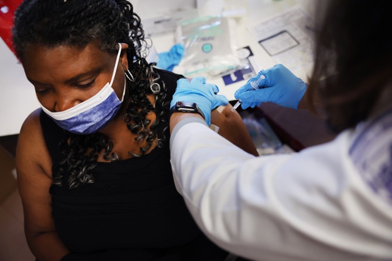 A woman wearing a surgical mask receives a COVID-19 booster vaccine designed to protect against the Omicron variant