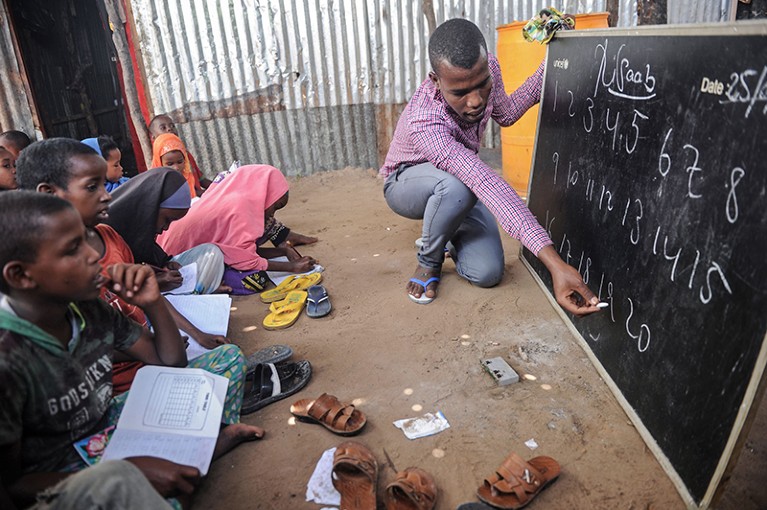 A university student and volunteer teacher, teaches displaced Somali children and teenagers at a chalkboard in Somalia, 2018.