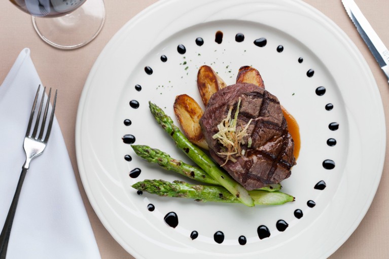 Overhead shot of a dining plate with a carefully arranged meal of beef steak, asparagus, potatoes and drops of balsamic vinegar