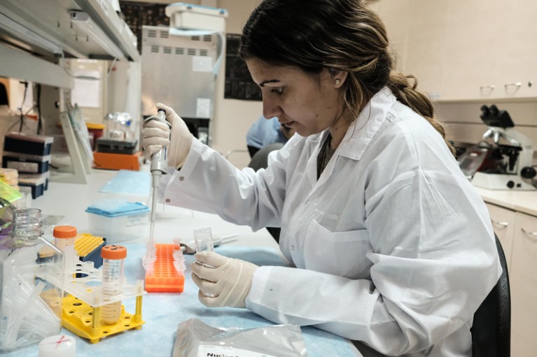 A woman wearing a white coat works at a bench in a lab.