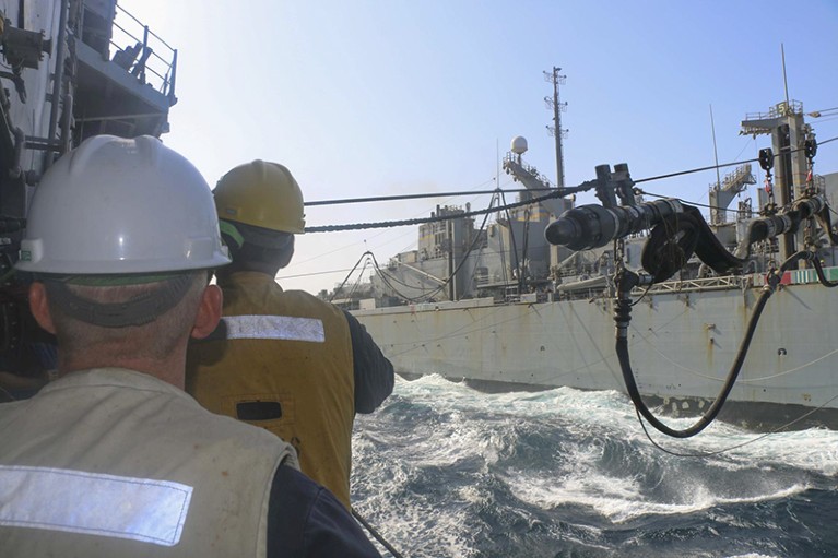Sailors on a US guided-missile cruiser observe a fuel probe from the fast combat support ship USNS Arctic during refueling.