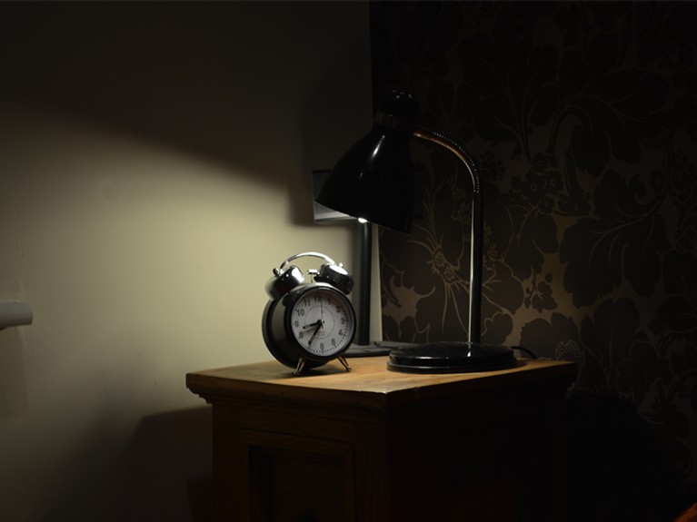 Lamp and alarm clock on bed table.