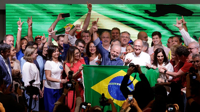 Lula in a crowd of smiling people, holding a Brazilian flag.